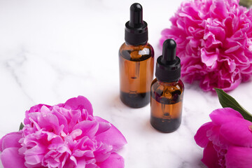 Glass dropper bottles on marble background with peony flower. Hyaluronic acid oil, serum with collagen and peptides skin care product. Mockup packaging, cosmetic design branding