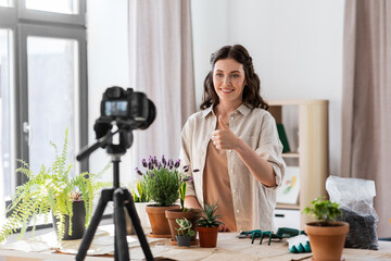 blogging, gardening and housework concept - happy woman or blogger with camera and pot flowers recording tutorial video and showing thumbs up at home