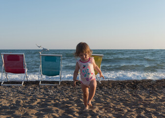 Little girl in sitting on sand and playing with bucket and spade at sea beach in warm sunny summer day. Closeup. Side view.