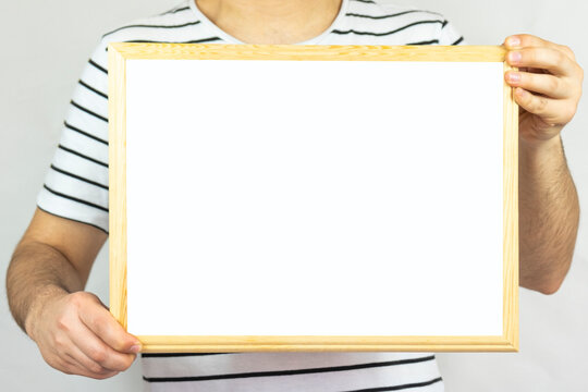 Young Man Holding Wooden Frame With Blank Area, Copy Space, Isolated On White Background, Paper Area For Text On A Wooden Pinboard, Banner Idea, Message Text Concept