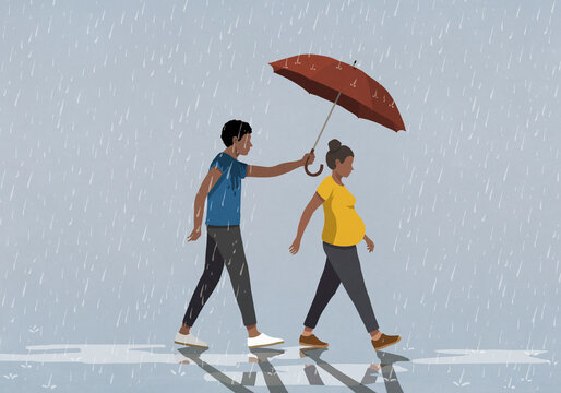 Husband holding umbrella over pregnant wife walking in rain

