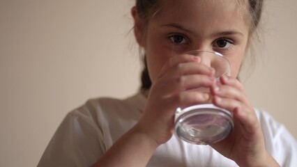 child drinking water. little girl in the kitchen drinks water from a glass cup. problem of shortage...