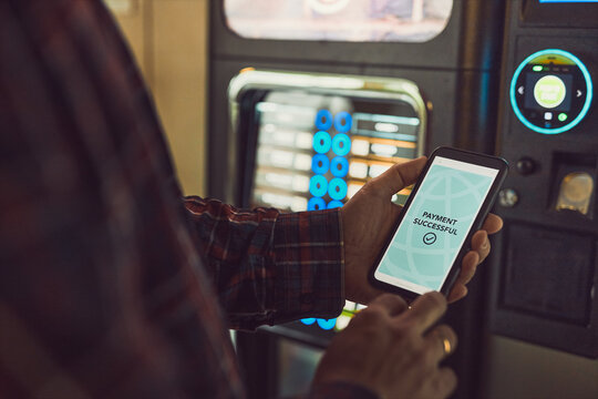 Consumer paying for product at vending machine using contactless method of payment with mobile phone. Man using payment app on smartphone to buy product
