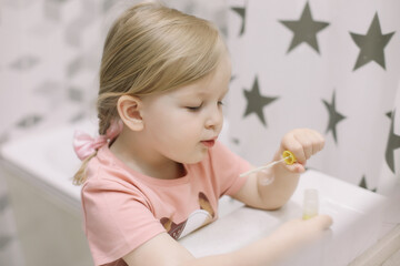 Fototapeta premium portrait of a cute baby girl playing with water and soap bubbles in a bath sink at home