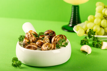 French cuisine Bourgogne Escargot Snails with garlic herbs butter in ceramics pan on green background with copy space