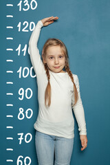 Cute little girl measuring height near blue wall background at home