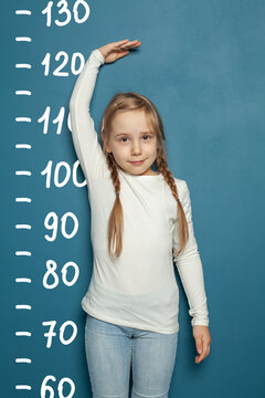 Cute little girl measuring height near blue wall background at home