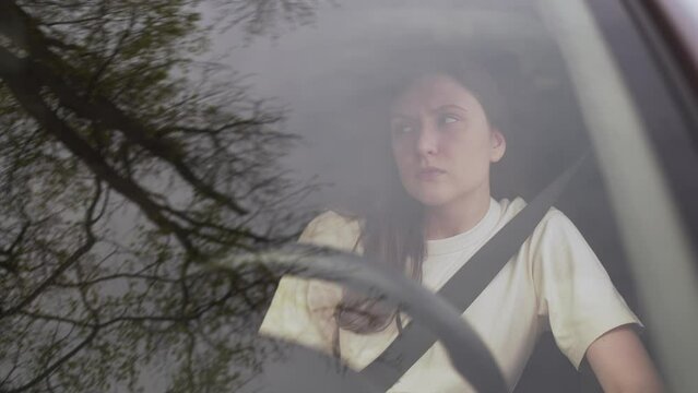 Depressed woman behind the wheel of a car, a view from behind the glass. Frustration and sadness 4K 10 BIT