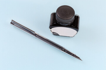 Modern fountain pen and glass ink vial on blue surface