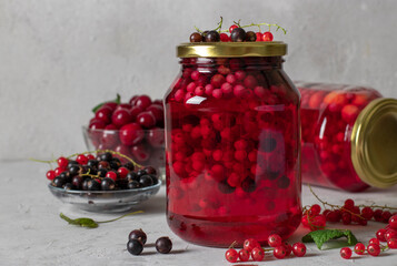 Homemade canned compote with cherries and currants in two jars on a light gray background.