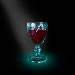 Green wineglass with dark red beverage illuminated by light beam on black background