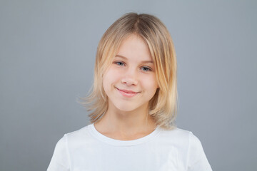 Happy little blonde kid girl in white t-shirt on gray background. Childhood lifestyle concept