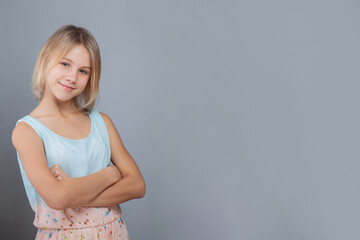 Happy child girl with blonde hair and cute smile posing on gray wall studio background
