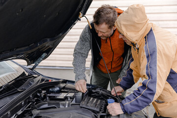 Fototapeta na wymiar Auto mechanics, Caucasian White mans, working in a car repair shop. Installing the new battery under the hood.