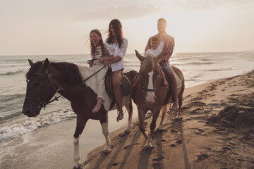 The family spends time with their children while riding horses together on a beautiful sandy beach on sunet. 