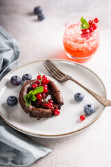 High angle view of warm chocolate pudding lava cake with fondant centre, red currants, bleuberry and mint leaves on gray background