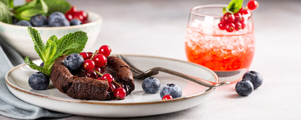 Banner with warm chocolate Lava Cake with bite taken out of molten center, red currants, bleuberry and mint leaves on gray background