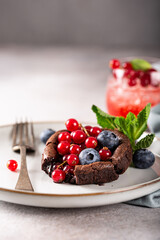 Delicious chocolate fondant or lava cake with red currants, bleuberry and mint on light grey concrete background. Hot chocolate dessert (pudding) with liquid center. Copy space