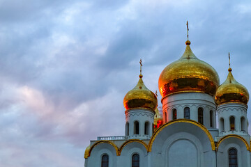 Fototapeta na wymiar golden domes of the white church with the reflection of the sun at sunset 