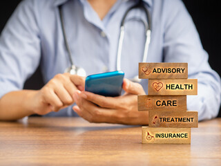 Wooden blocks with health icons and the letters Advisory, Health, Care, Treatment, and Insurance over a wooden desk with a doctor sitting blurred background