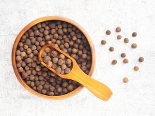 Spice Allspice (Jamaica pepper, Pimento) in wooden bowl, scoop, bunch on white concrete background. Macro. Flat lay. Indian cuisine concept