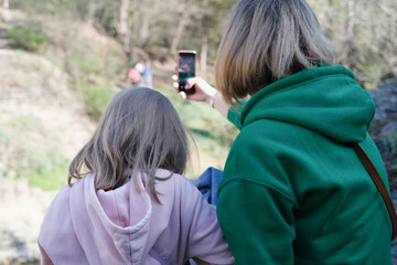 Mom and daughter sit with backs and take pictures of nature on smartphone