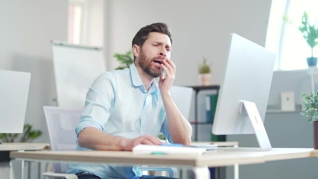 Bored sleepy office worker sitting at work workplace at computer desk leaning on hand yawning. Tired man. Exhausted Businessman employee. Portrait Depressed, unhappy, workless male manager. indoor