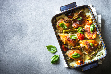 Baked chicken thighs with asparagus and tomatoes in a creamy sauce. Top view with space for text.4