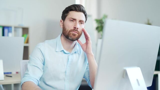 Focused confident handsome bearded business man looks at screen computer monitor or laptop at work in the office. Close up of thoughtful employee entrepreneur in smart casual browsing typing Indoor