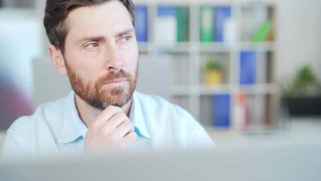 Portrait close up of pensive thinking handsome bearded man in front of laptop computer monitor at workplace in office. face thoughtful focused mle copywriter sitting at desk. Business People and work