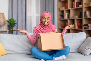 Overjoyed african american muslim lady opening cardboard box, receiving online shop order at home,...