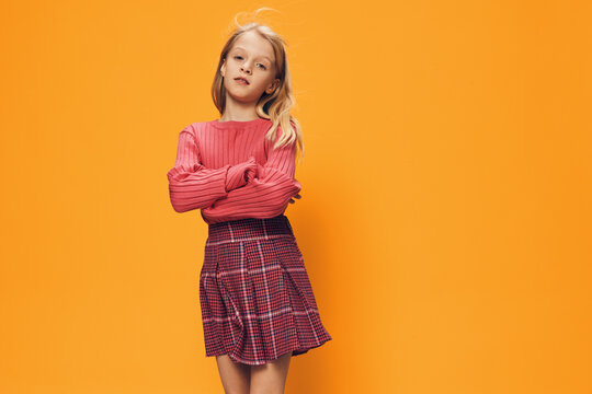 beautiful cute girl in bright clothes stands on a yellow background with her arms folded on her chest