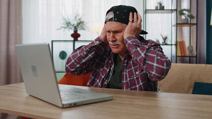 Stressed senior grandfather working on laptop computer at home office. Upset man received bad news....