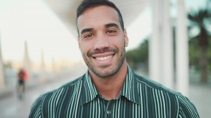 Handsome brunette man turning his head and smiling at camera outdoors. Young businessman dressed in shirt looking confident posing on the street - Powered by Adobe