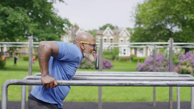 Muscular and healthy senior black male doing tricep dips on bars in an outdoor gym