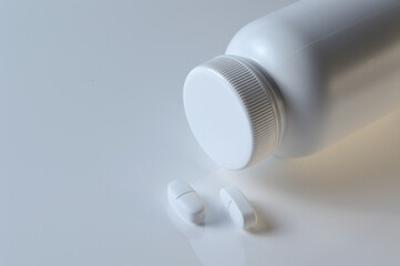 white plastic medicine jar and two white pills. light background