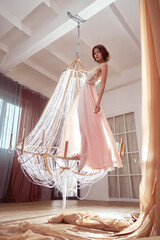 Art beauty woman in long beige pink dress dances and spins on large crystal chandelier in center of...