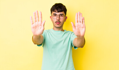 young adult hispanic man looking serious, unhappy, angry and displeased forbidding entry or saying...
