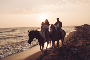 The family spends time with their children while riding horses together on a beautiful sandy beach on sunet. 