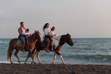 The family spends time with their children while riding horses together on a sandy beach. Selective focus 