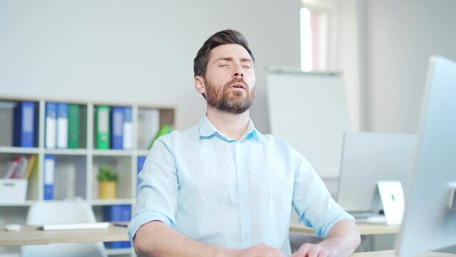 Male worker relaxes with eyes closed and takes a deep breath. enjoys the cold and fresh air in the room. Sitting on workplace in the office indoors at work. Man employee entrepreneur a computer desk