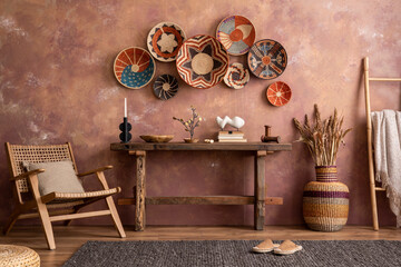 The stylish ethnic compostion at living room interior with wicker baskets, wooden bench, armchair...