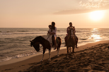 The family spends time with their children while riding horses together on a sandy beach. Selective focus 