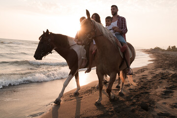 The family spends time with their children while riding horses together on a sandy beach. Selective focus 