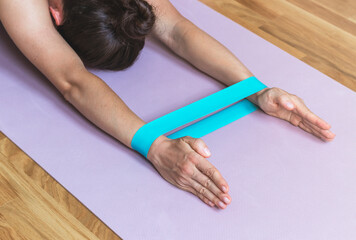 Woman doing yoga on an exercise mat with a rubber resistance band on her hands.