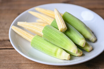 Fresh young baby corn for cooking health food, Close up raw organic baby corn on wooden background, Baby corn on white plate.