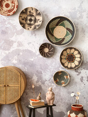 The stylish ethnic composition at living room interior with colorful baskets, rattan sideboard, black stool and elegant personal accessories. Grey concrete wall. Cozy apartment. Home decor.