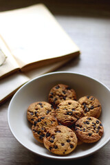 Plate of chocolate chip cookies, open books and reading glasses on wooden table. Selective focus.
