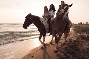The family spends time with their children while riding horses together on a beautiful sandy beach on sunet. 