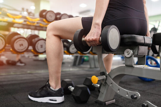 Adult athletic woman in black sportswear performs strength training in the gym. Girl lifts heavy weights on the background of sports equipment. Theme of health, sports lifestyle.